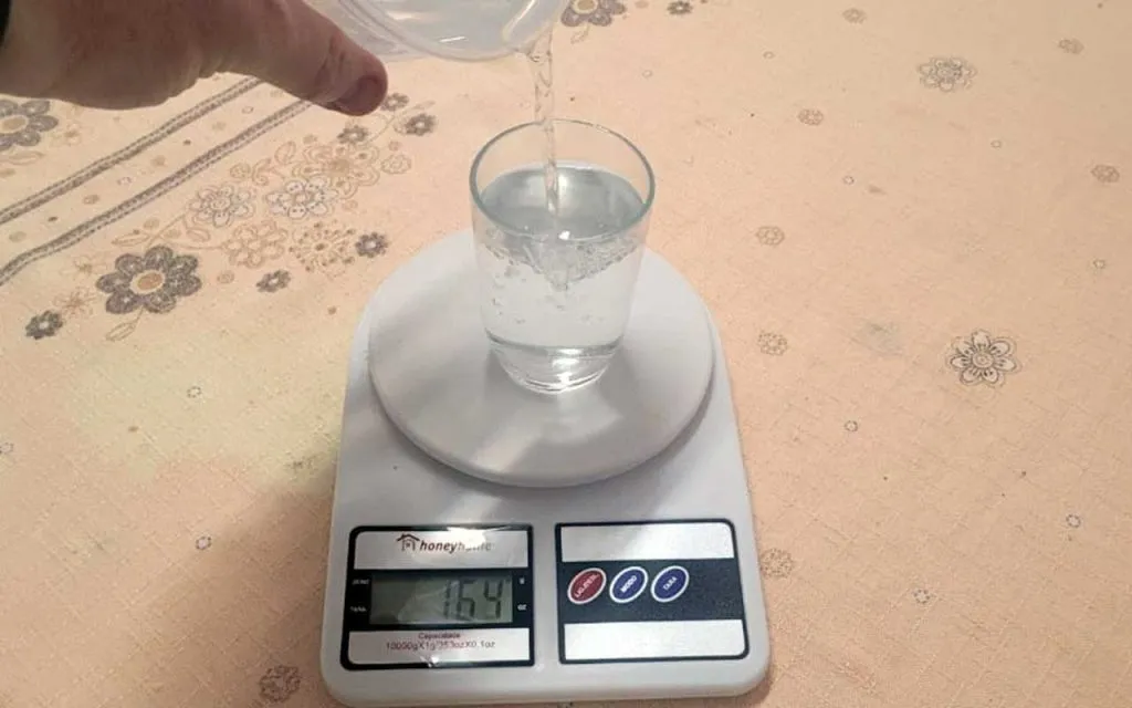 Copo americano em cima de uma balança de cozinha medindo água para uma receita